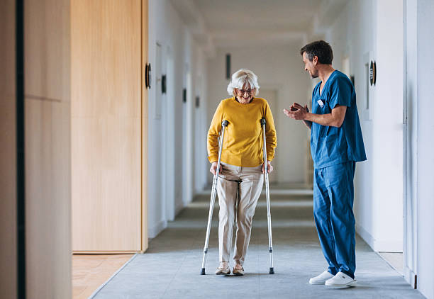 A healthcare professional walking alongside a patient using crutches in a hospital corridor
