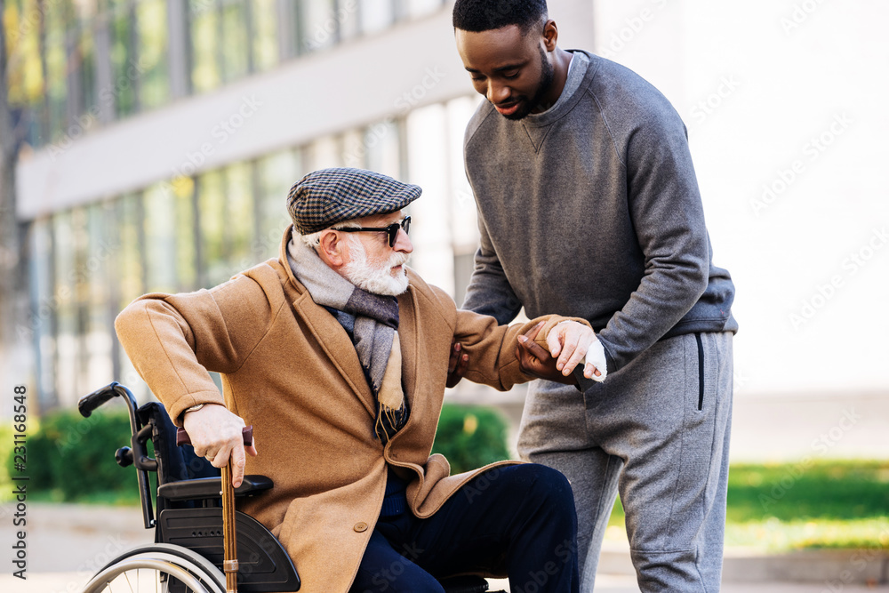 A young man assisting an older adult in a wheelchair outdoors